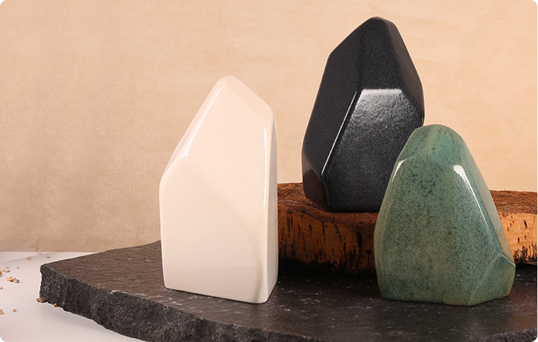 Ceramiczne urny Orion — trzy obiekty w kolorach białym, czarnym i zielonym na kamiennej podstawie